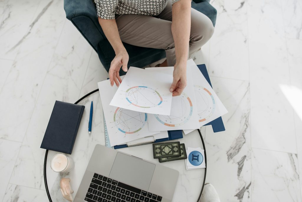 Astrology charts displayed with a laptop, deck of cards, and stationery on a marble floor.